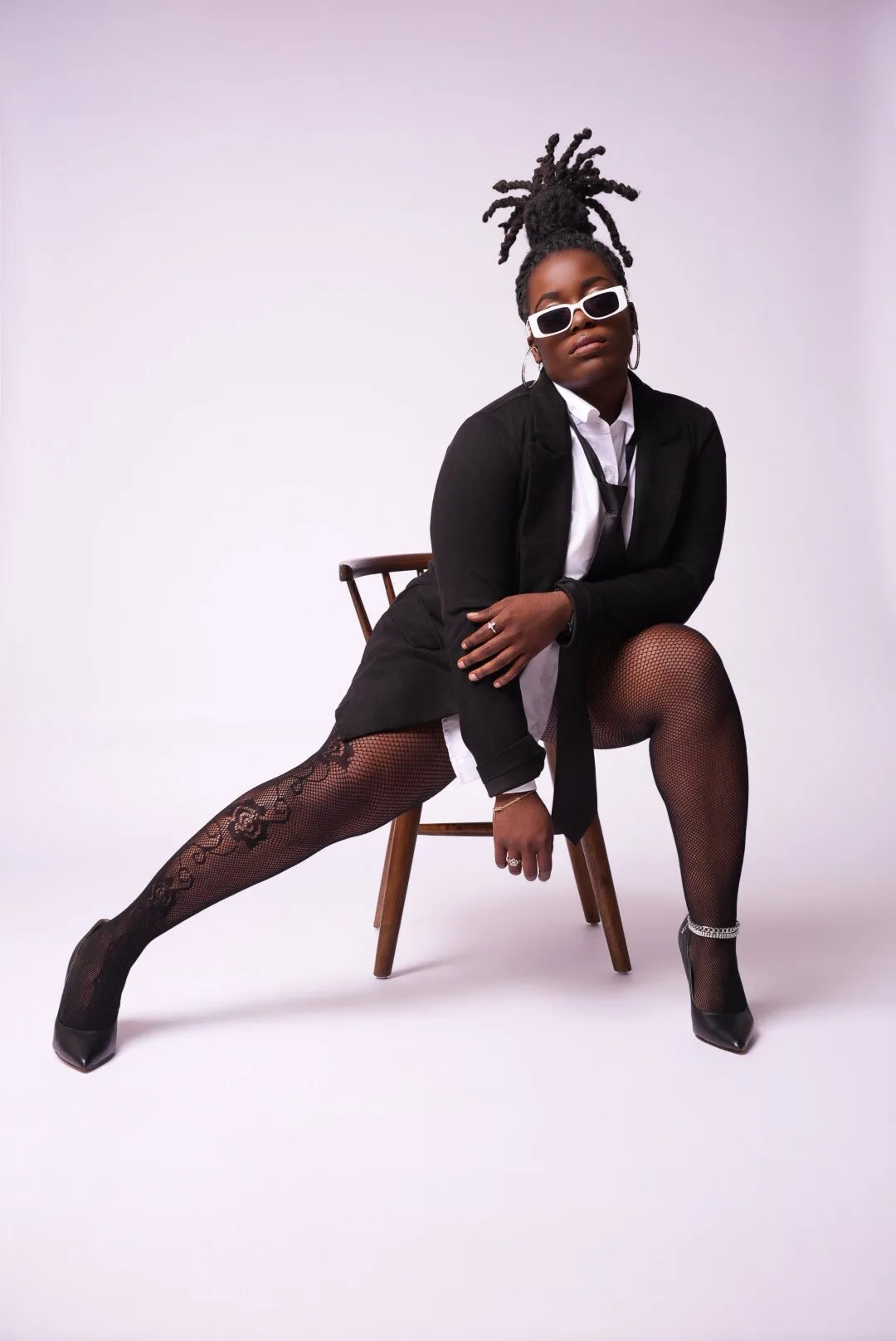 Editorial portrait seated in a black suit and sunglasses